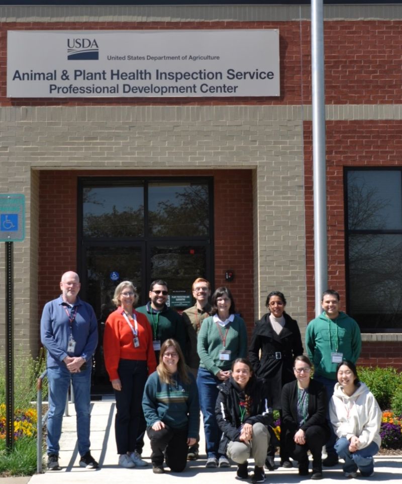 A small group of people, some kneeling, in front of a brick building.