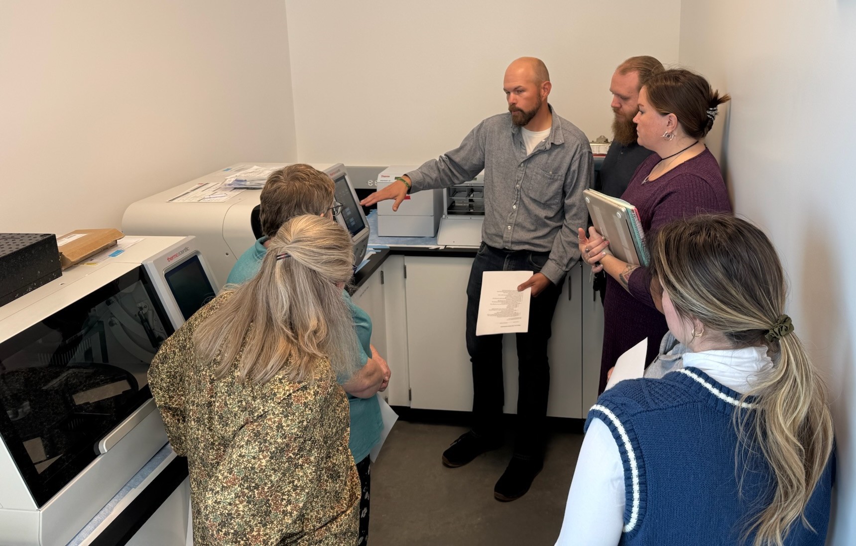 A man showing a group of people the read outs on a piece of lab equipment